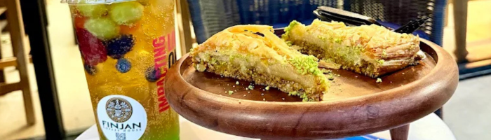 Pistachio baklava on a wooden tray beside a Finjan iced drink